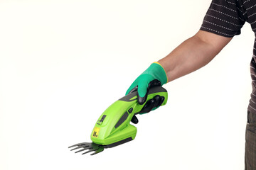 Hand in protective glove holds an electric garden trimmer for trimming bushes and plants. On light...