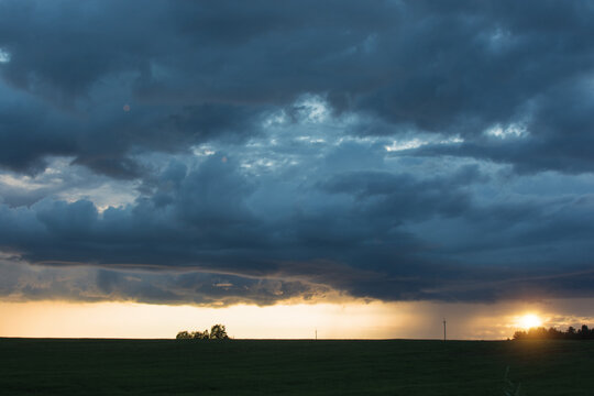Huge, blue storm clouds in the setting sun. Contrasting rural landscape. An impending storm. Horizontal photo.