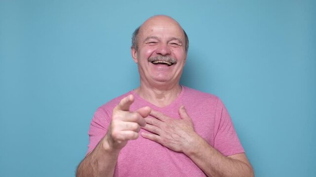 Senior hispanic man laughing at you, pointing finger to the camera
