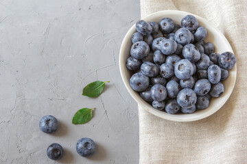 Fresh blueberries in white bowl. Fresh blueberries with green leaves on gray table. Concept for healthy eating and nutrition. Top view. Copy space.