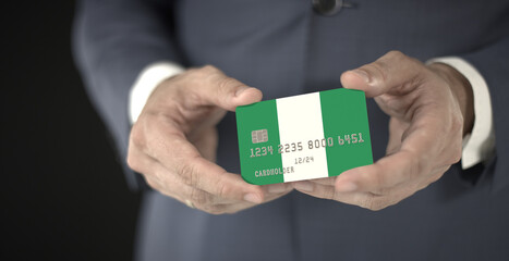 Businessman holding plastic bank card with printed flag of Nigeria, fictional numbers