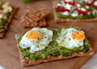 Avocado Toast with fried eggs. Colorful avocado toast over a wooden cutting table. Rustic mood. Close up. Selective focus.