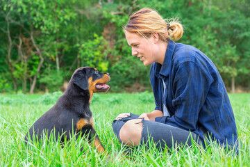 Young woman sitting with rottweiler puppy in meadow
