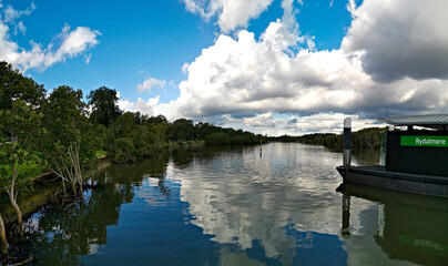 Fototapeta premium Beautiful view of a river and a wharf with reflections of blue sky, light clouds and trees on water, Parramatta river, Rydalmere, New South Wales, Australia