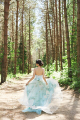 Pretty brunette woman in a long dress running away in summer forest