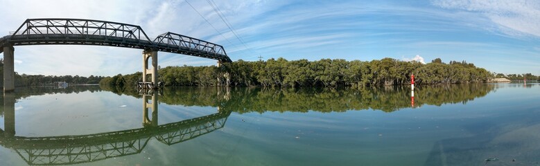 Beautiful panoramic view of a river with reflections of tall pedestrian bridge, trees and blue sky, Parramatta river, Rydalmere, New South Wales, Australia