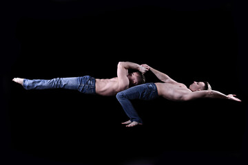 two twin brothers in blue jeans with a naked torso perform acrobatic elements, black background