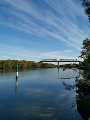 Fototapeta premium Beautiful view of a river with reflections of tall pedestrian bridge, trees and blue sky, Parramatta river, Rydalmere, New South Wales, Australia