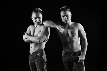 Fototapeta na wymiar two twin brothers in blue jeans with a naked strong torso posing. black and white 
