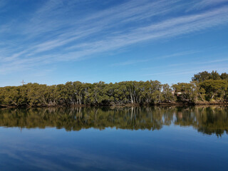 Fototapeta na wymiar Beautiful view of a river with reflections of blue sky, light clouds and trees on water, Parramatta river, Rydalmere, New South Wales, Australia