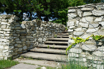 old stone and wooden steps overgrown with vegetation, leading up. Clear sunny summer day.