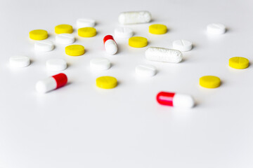 Multicolored tablets and pills scattered on white table. Pharmaceutical drug isolated copy space minimalistic background