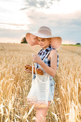 Naklejka na ściany i meble Happy girl walking in golden wheat,with her back, outdoor lifestyle. Freedom concept. Cute little girl in summer field.takes bread from an eco bag, string bag in his hands