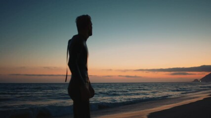 Silhouette of surfer turning back to see a sunset, walking out of water after surfing training, sunset over the Pacific ocean