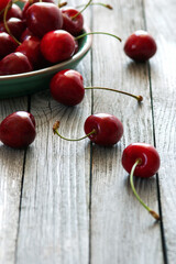 red cherries in ceramic plate on wooden table, vertical shot