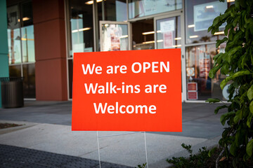 Red sign at a salon stating  We are OPEN Walk-ins Welcome during coronavirus pandemic .