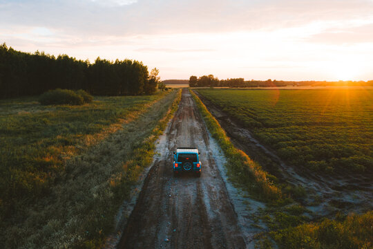 Aerial view of suv vehicle driving on countryside road during sunset in summer.