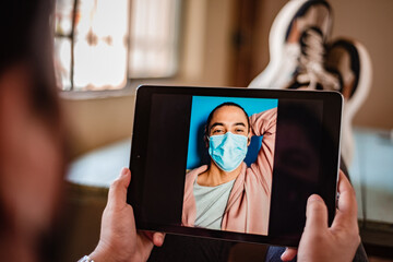Latino young man in medical mask has a video call from a tablet with his girlfriend. Coronavirus concept