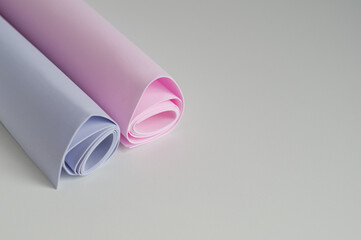 Two rolled-up sheets of pink and blue textured paper. Pastel colors, gray background, horizontal photography.