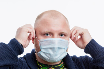 A bald man puts on a medical mask. Close-up. Isolated on white background. Coronavirus pandemic.