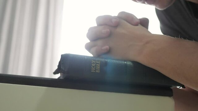 man praying indoors at bedtime on bible. religion concept evening prayer human brunette hands lifestyle bible praying by bed