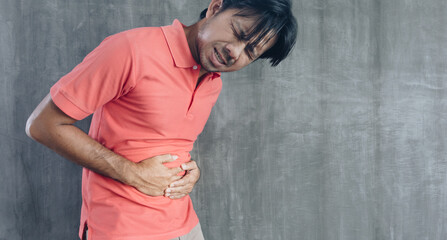 Young asian man having a stomach ache on Cement wall background, Problems and health care concepts