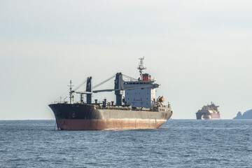 Old commercial cargo ship with heavy cranes anchors in the sea.