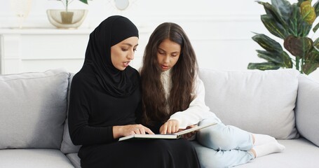 Young beautiful Arabian woman in black hijab trading interesting story in book for pretty small...