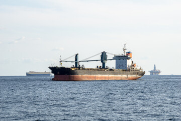 Old commercial cargo ship with heavy cranes anchors in the sea.