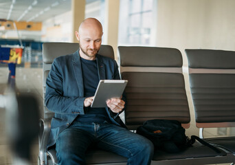 Handsome adult bald bearded man businessman in suit using tablet at the airport lounge
