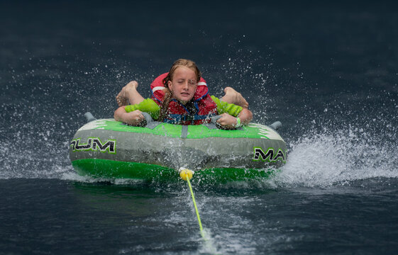 A girl being towed behind an inflatable sea biscuit on a lake with dark water