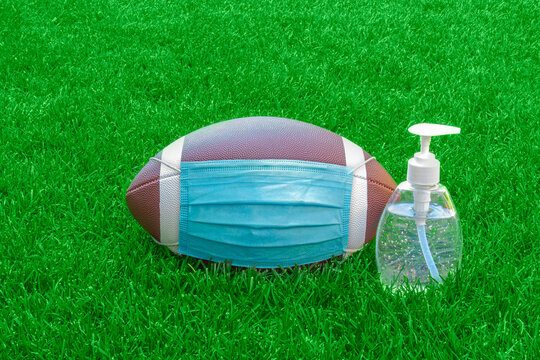 An American Football with a face mask and hand sanitizer on the right on field with green grass. Concept Football during pandemic
