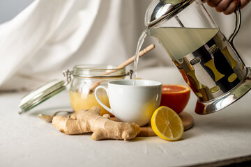 Fototapeta na wymiar Person is pouring in a cup of vitamin warming tea with ginger, lemon and honey. Concept of useful and tasty tea in the cold days or with the flu