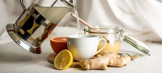 Person is pouring in a cup of vitamin warming tea with ginger, lemon and honey. Concept of useful and tasty tea in the cold days or with the flu