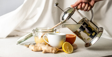 Person is pouring in a cup of vitamin warming tea with ginger, lemon and honey. Concept of useful and tasty tea in the cold days or with the flu