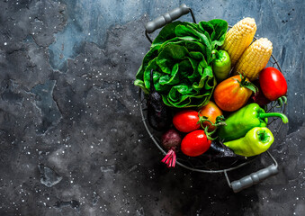 Raw vegetables. Eggplant, zucchini, tomatoes, corn, pepper, lettuce in a vintage metal basket on a dark background, top view. Copy space