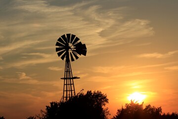 windmill at sunset with tree's,clouds, and the Sun north of Hutchinson Kansas USA out in the country.