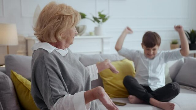 Blonde old grandmother looking after hyperactive energetic teen child boy shrugging shoulders at camera feel confused. Funny scene. Family. Upbringing.
