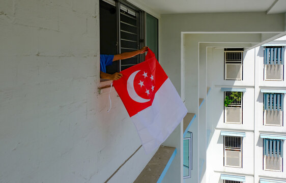 Person hanging Singapore flag outside apartment windows, to welcome national day