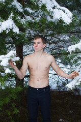 young man without a shirt in the winter forest sprinkles snow