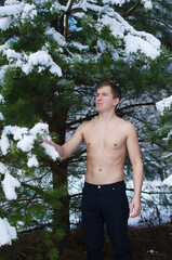 young man without a shirt in the winter forest sprinkles snow