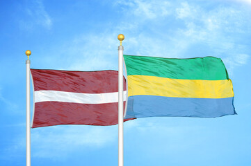 Latvia and Gabon two flags on flagpoles and blue sky