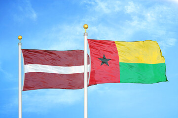 Latvia and Guinea-Bissau two flags on flagpoles and blue sky