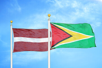 Latvia and Guyana two flags on flagpoles and blue sky