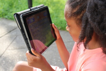 Young Black Kid holding table electronic device outdoors on summer day close up 
