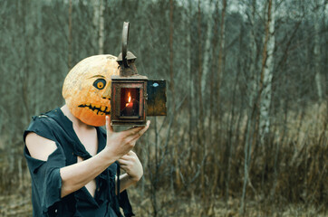 man in ragged clothes holding a Halloween lantern stares into the flames of a pumpkin Jack candle