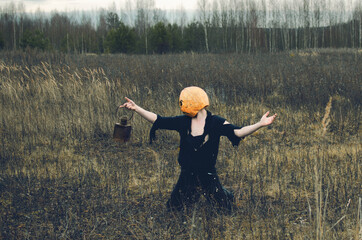 man in ragged clothes with a lantern and a Halloween mask on his head is kneeling in an autumn field. pumpkin Jack