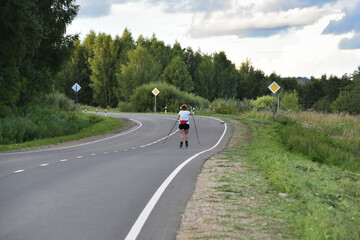 A woman on roller skis is rolling along an asphalt country road.