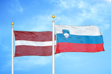 Latvia and Slovenia two flags on flagpoles and blue sky