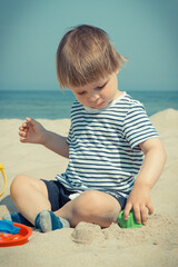 Baby boy playing with sand on summer beach. Vacation time and child development concept